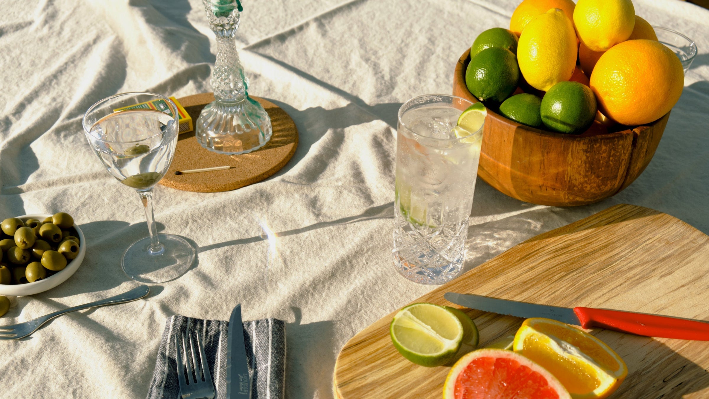 A close-up of a table spread with fresh citrus fruits, green olives, and a sparkling Devon Gin cocktail, highlighting the natural ingredients and sophisticated style of Good Natured Spirits.