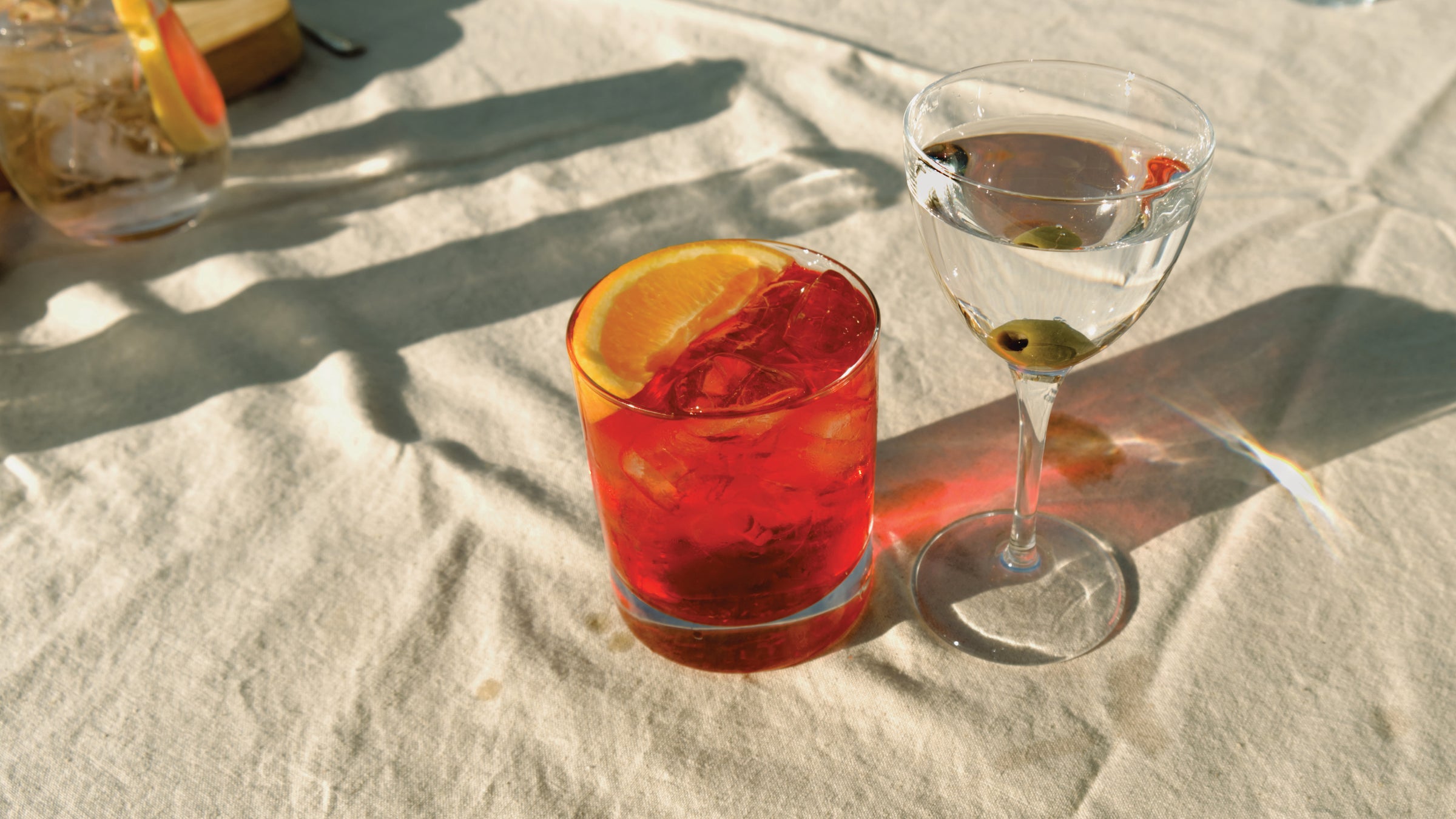 A vibrant and enticing negroni cocktail made with Good Natured Spirits Devon gin, accompanied by a martini made with Copper Frog Gin with olives on a white linen tablecloth.